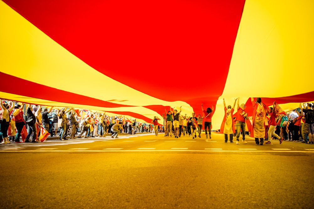 Demonstrators against Catalan independence tendencies enjoy running under a giant half Spanish half Catalan flag during a manifestation on columbus day at Catalonia square in Barcelona