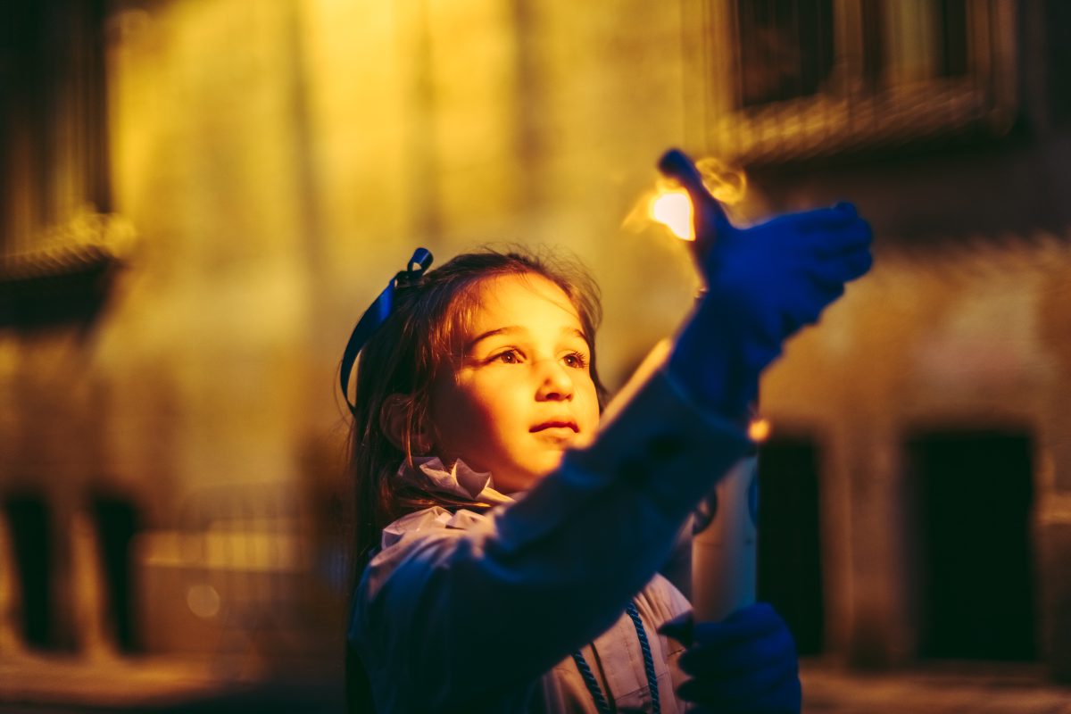 Tarragona, Spain. 7 April, 2023: A little girl from the 'Cofradia Dels Pescadors' brotherhood shields with her hand a candle against the wind during the procession Good Friday procession in Tarragona.
