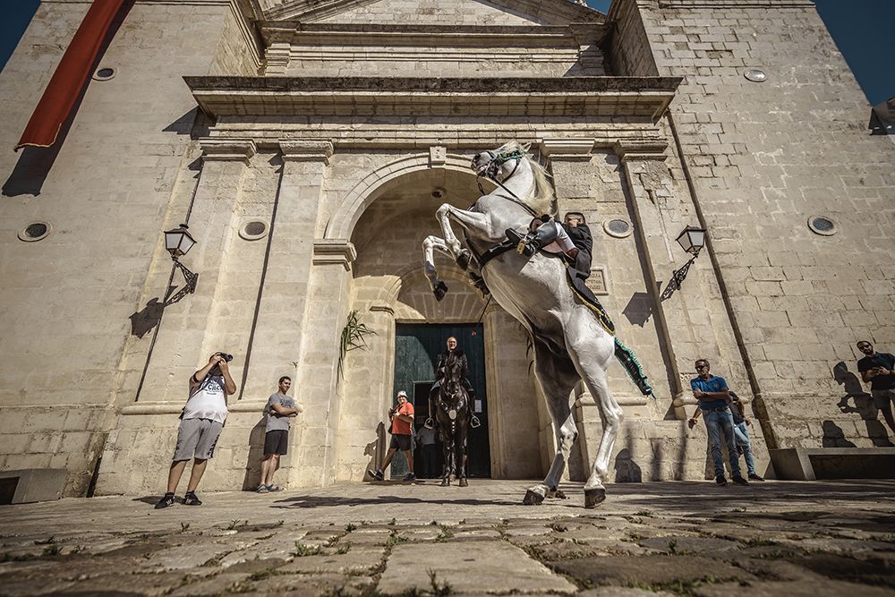 A 'caixer' (horse rider) rears up on his horse passing the greeting preast in his house before incorporating him into the cavalcade through the village prior to the traditional 'Jaleo' at the Sant Jaume Festival in Es Castell